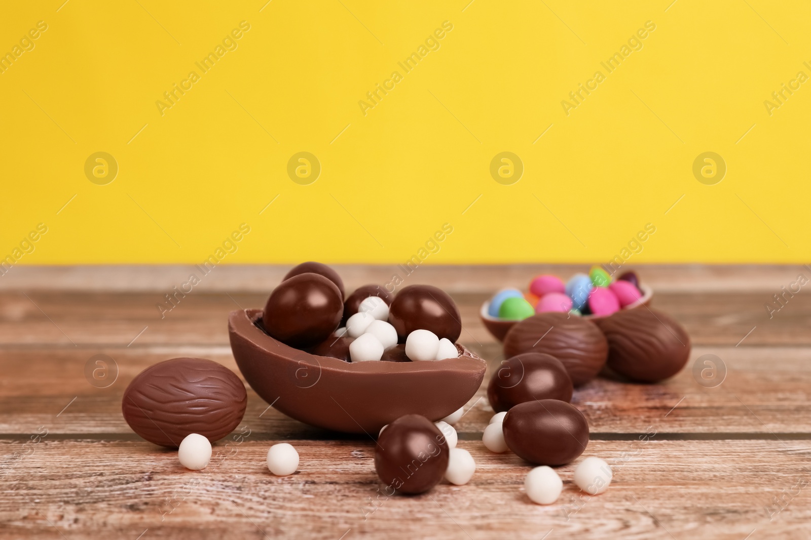 Photo of Delicious chocolate eggs and candies on wooden table against yellow background