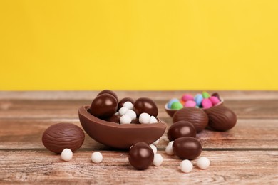 Delicious chocolate eggs and candies on wooden table against yellow background