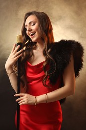 Photo of Beautiful young woman in stylish dress with microphone singing on dark background in color lights and smoke