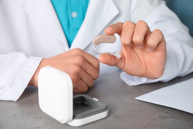 Photo of Doctor holding hearing aid at table, closeup. Medical device