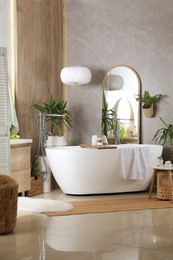 Modern white tub and beautiful green houseplants in bathroom. Interior design