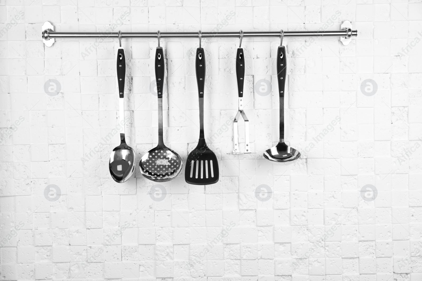 Photo of Rack with clean kitchen utensils on white wall