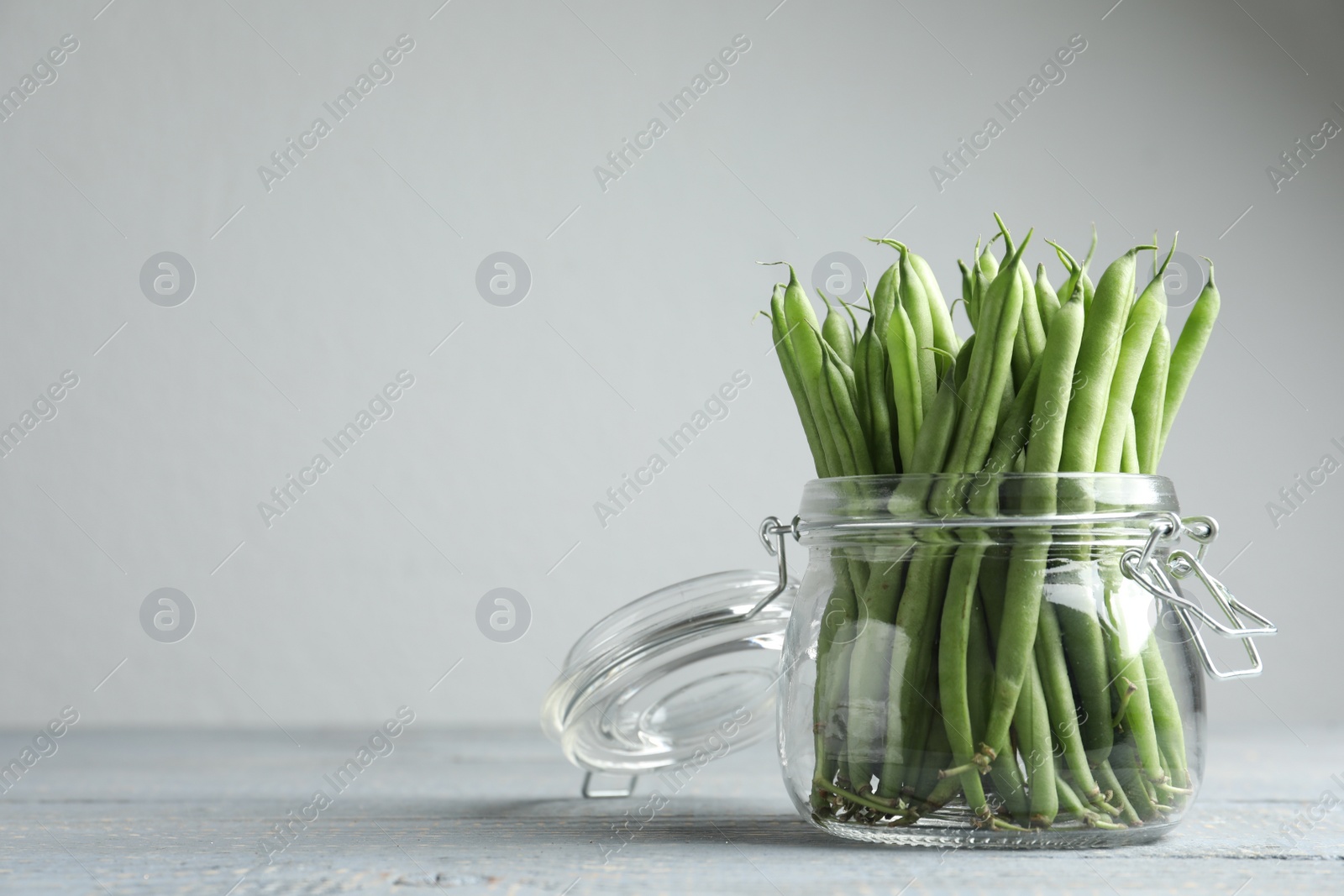 Photo of Fresh green beans in glass jar on grey wooden table, space for text