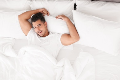 Photo of Young man lying in bed with soft pillows at home, top view