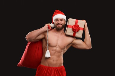 Photo of Attractive young man with muscular body holding bag and Christmas gift box on black background