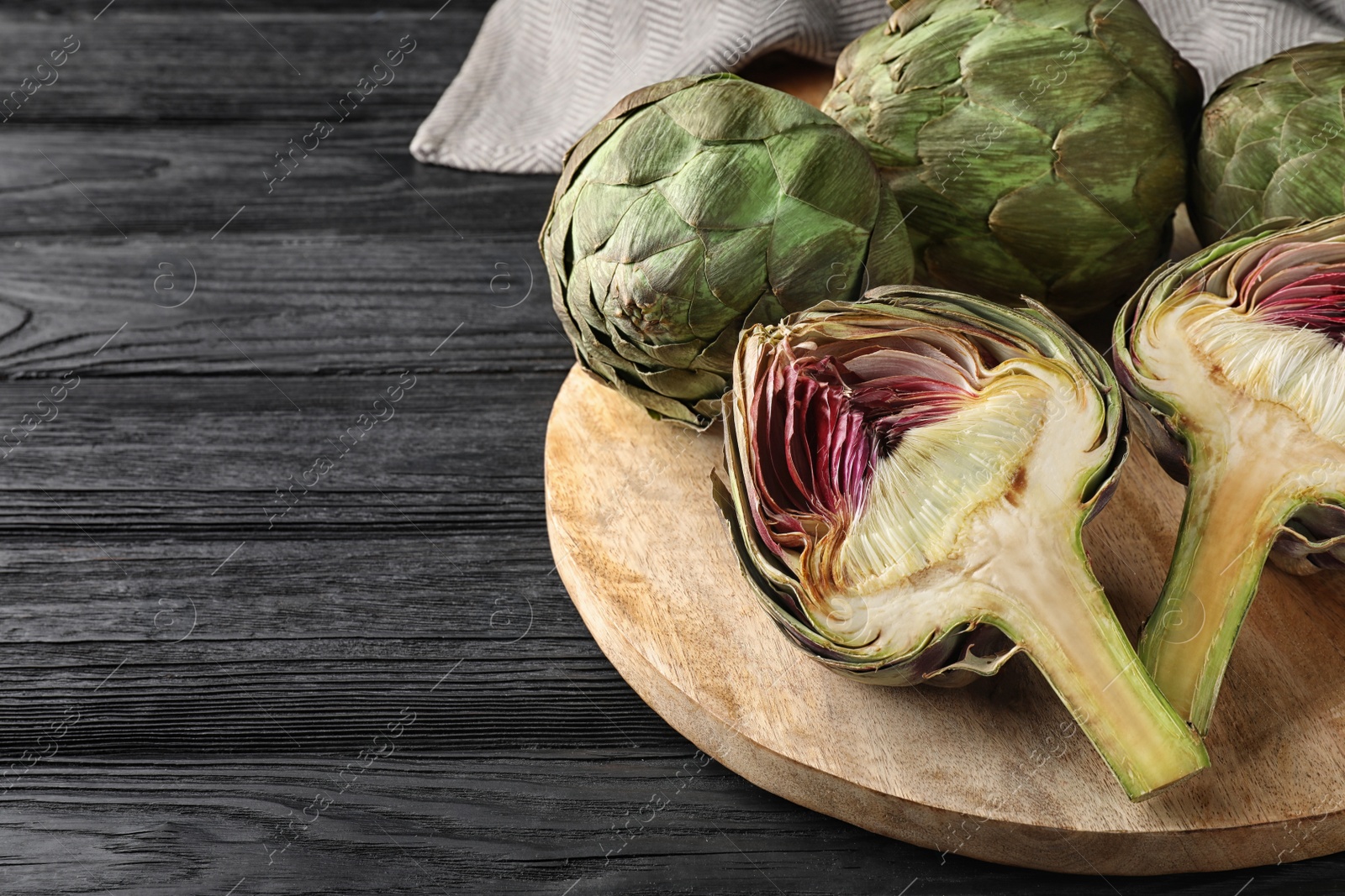 Photo of Cut and whole fresh raw artichokes on black wooden table, space for text