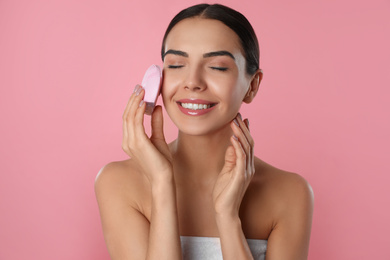 Photo of Young woman using facial cleansing brush on pink background. Washing accessory