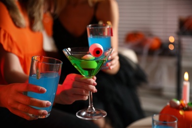 Photo of Group of friends toasting with cocktails at Halloween party indoors, closeup