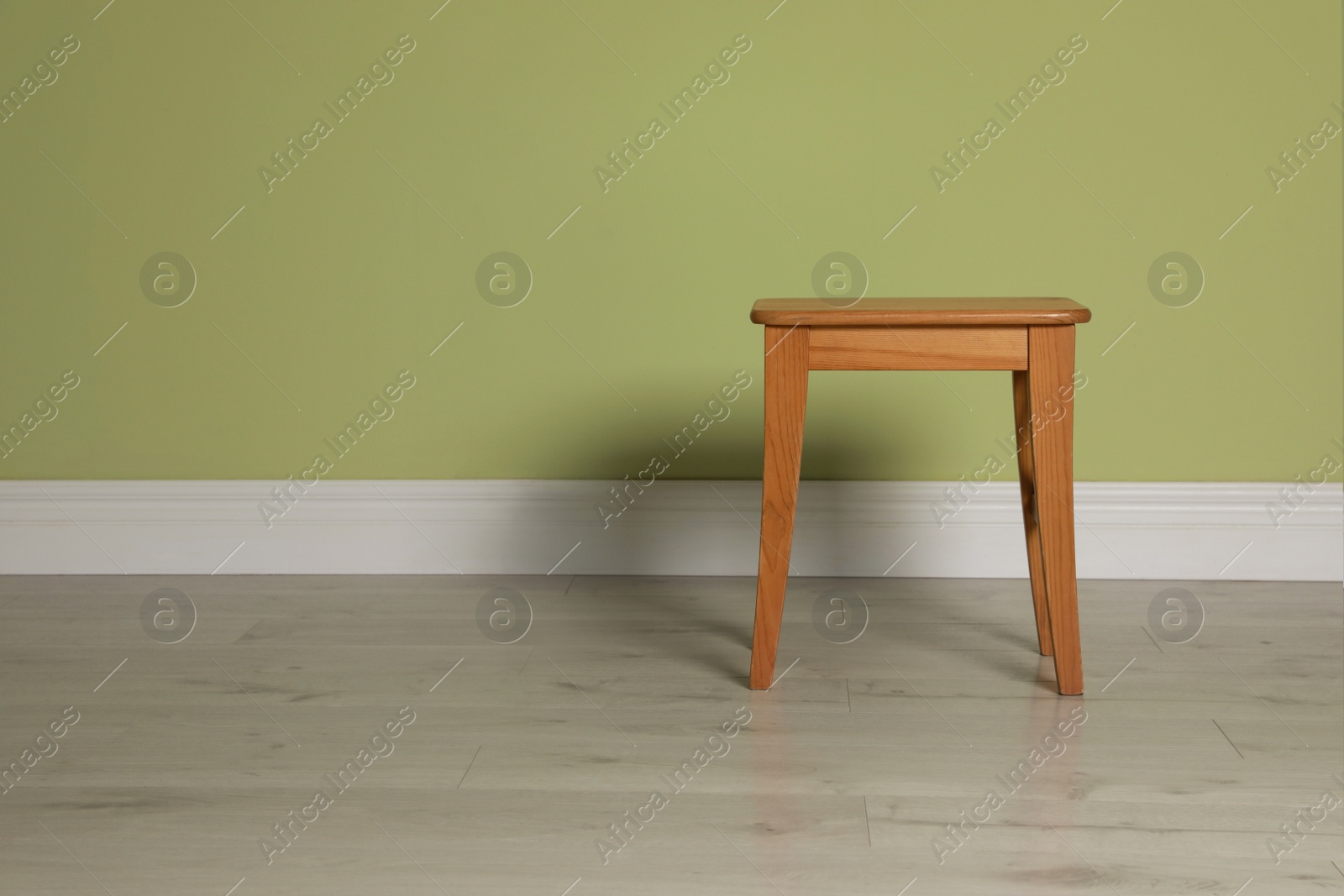 Photo of Stylish wooden stool near light green wall indoors. Space for text