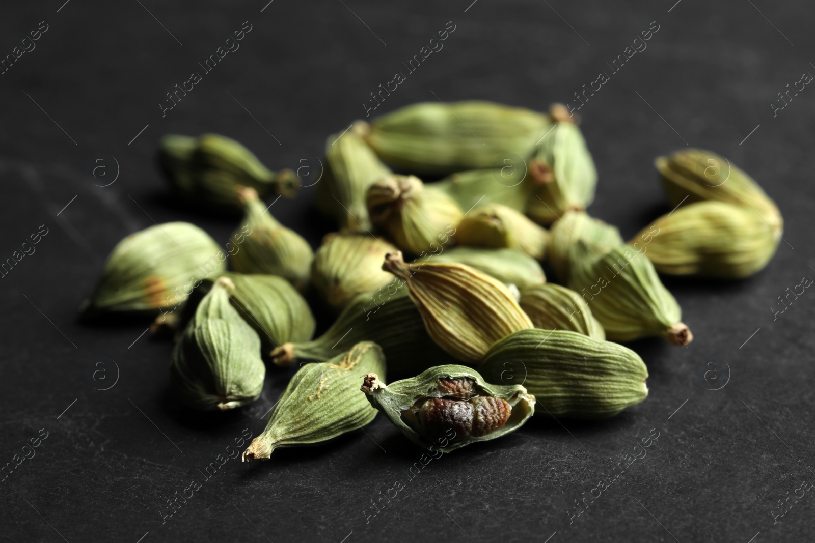 Photo of Pile of dry cardamom pods on black table, closeup