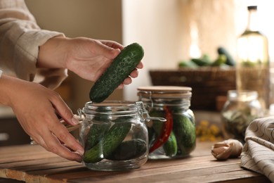 Photo of Woman putting cucumbers into jar at wooden table, closeup. Pickling vegetables