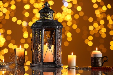 Arabic lantern and burning candles on mirror surface against blurred lights