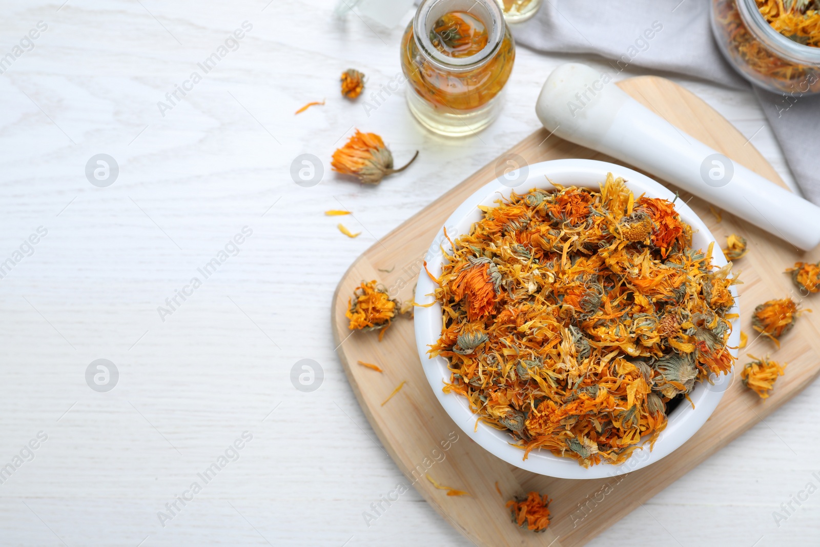 Photo of Dry calendula flowers and bottles with tincture on white wooden table, flat lay. Space for text