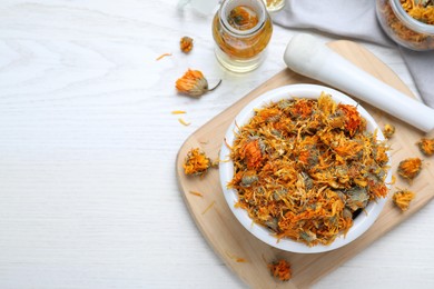 Dry calendula flowers and bottles with tincture on white wooden table, flat lay. Space for text