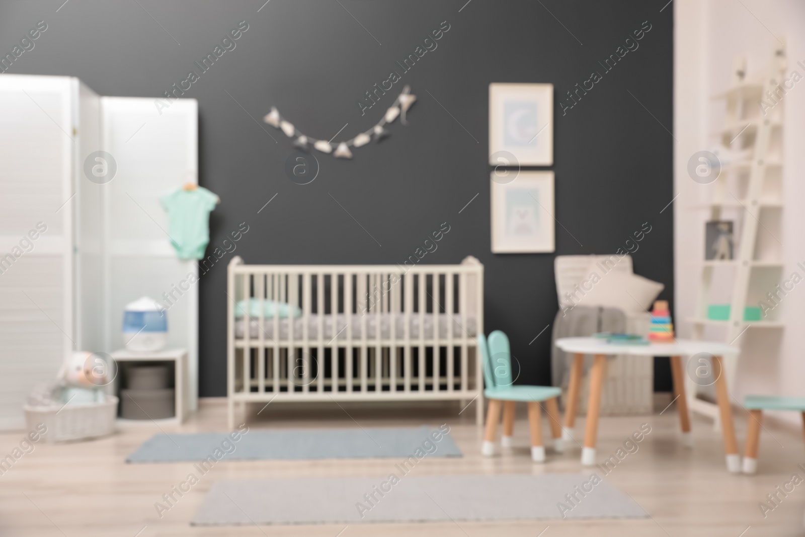 Photo of Blurred view of cute baby room interior with modern crib near dark wall