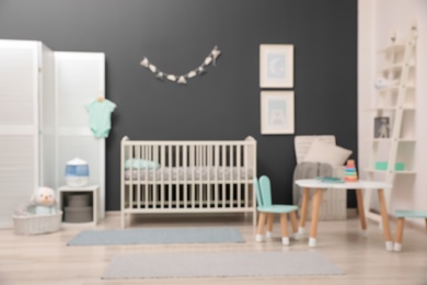 Photo of Blurred view of cute baby room interior with modern crib near dark wall