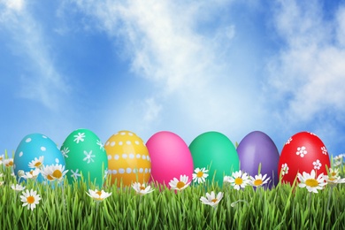 Image of Bright Easter eggs and spring flowers on green grass outdoors