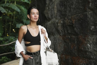 Beautiful young woman near stone wall outdoors, space for text