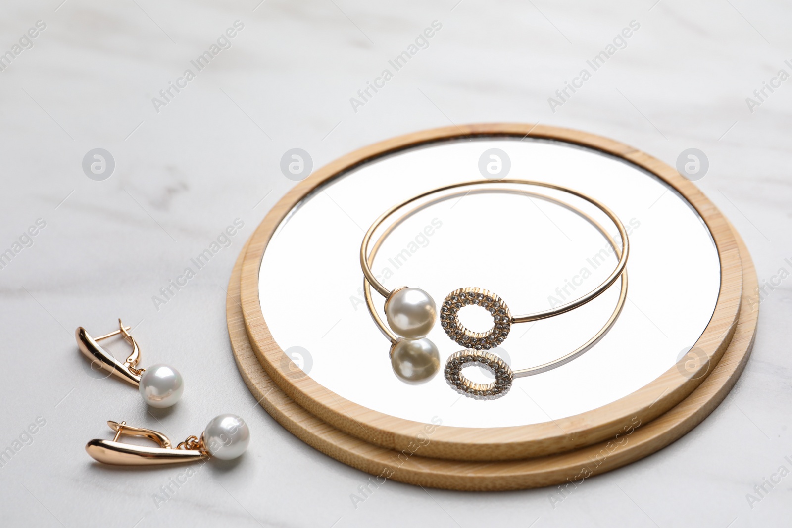 Photo of Elegant bracelet and earrings with pearls on white marble table