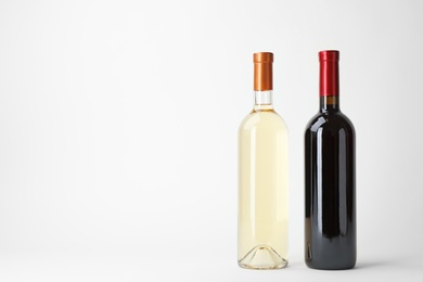 Photo of Bottles of expensive red and white wines on light background