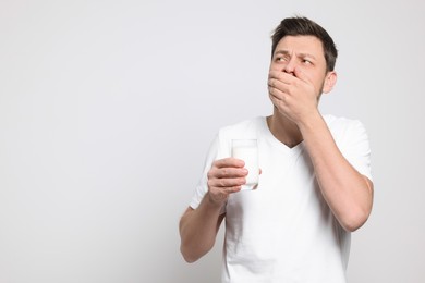 Man with glass of milk suffering from lactose intolerance on white background, space for text