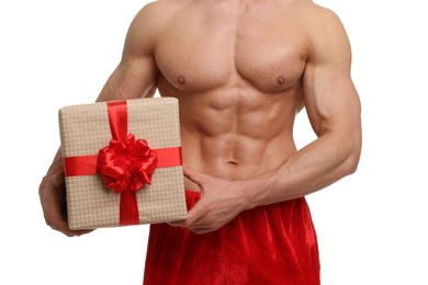 Attractive young man with muscular body in Santa hat holding Christmas gift box on white background, closeup