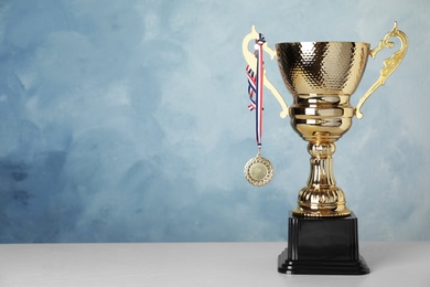 Photo of Golden trophy cup and medal on table against blue background. Space for text