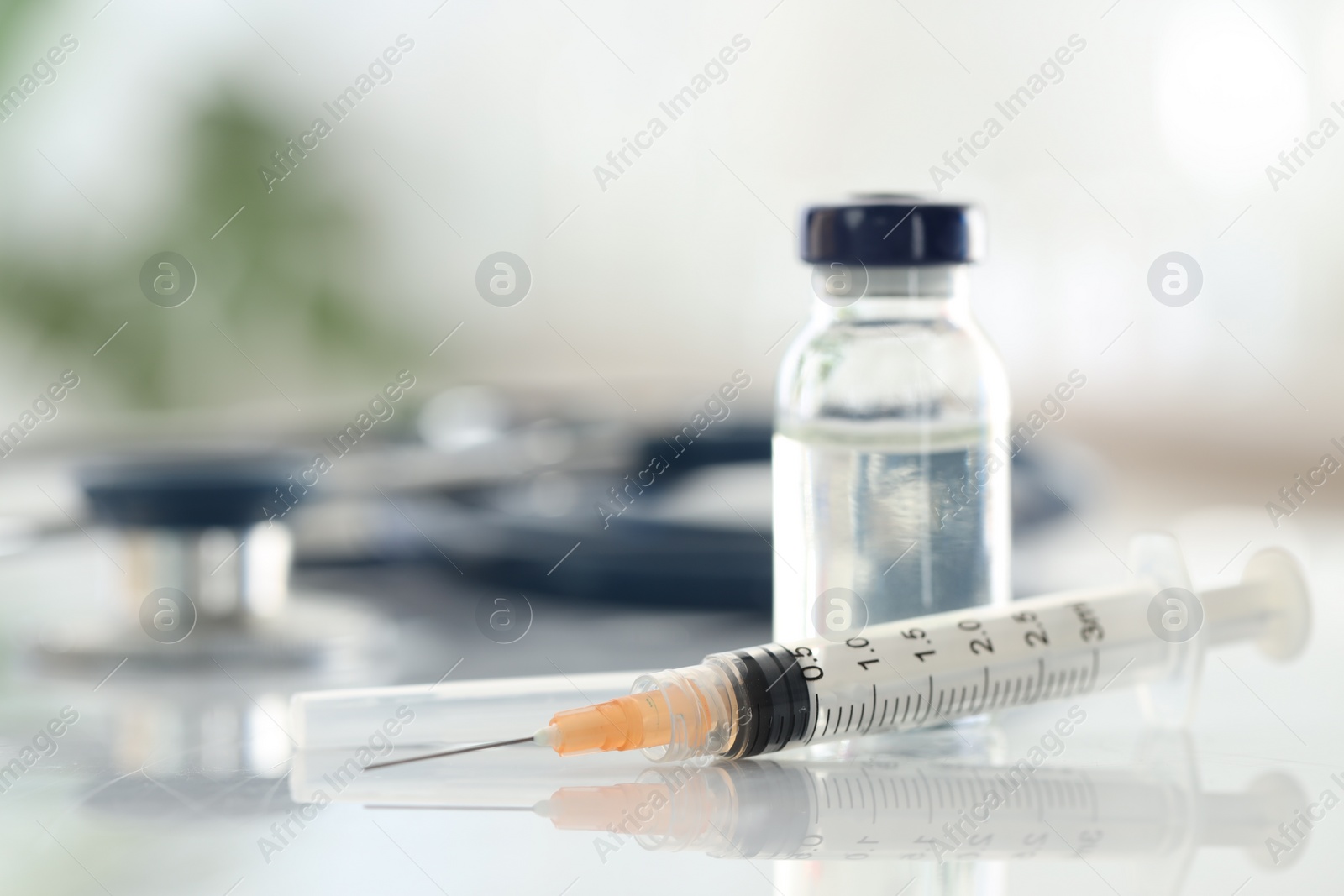 Photo of Glass vial, syringe and stethoscope on white table, closeup