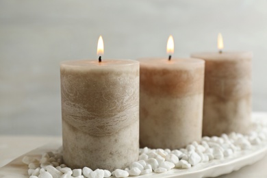 White plate with three burning candles and rocks on table