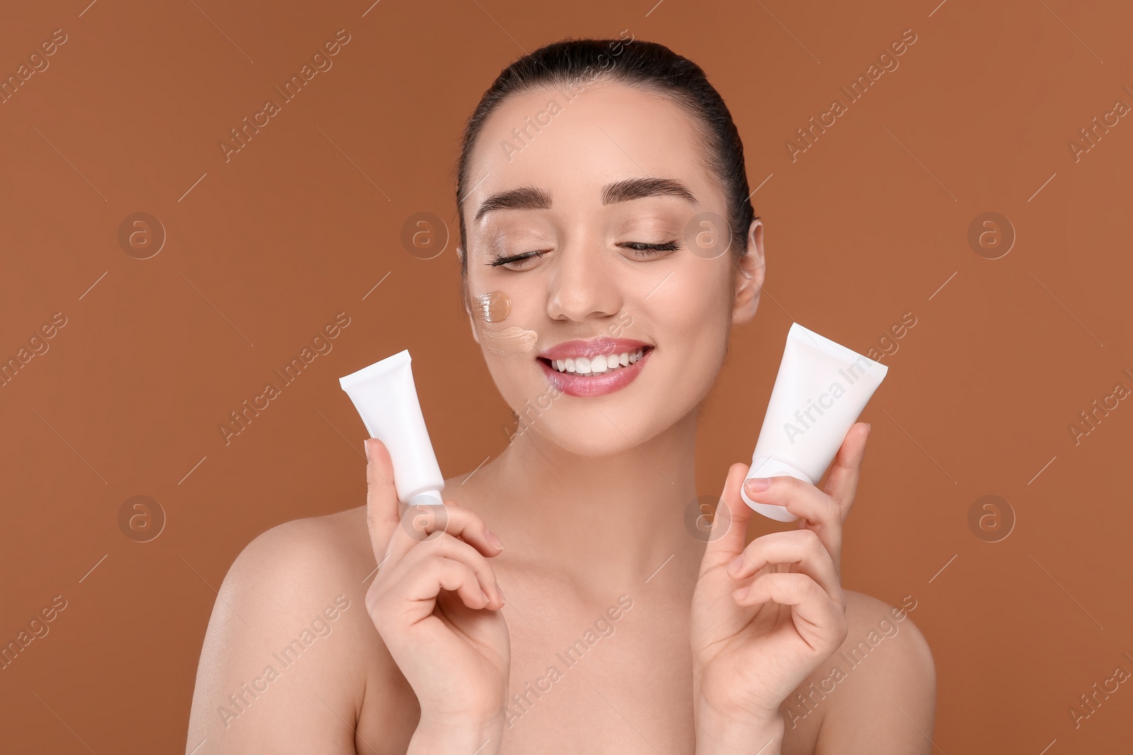 Photo of Woman holding tubes of foundation on brown background