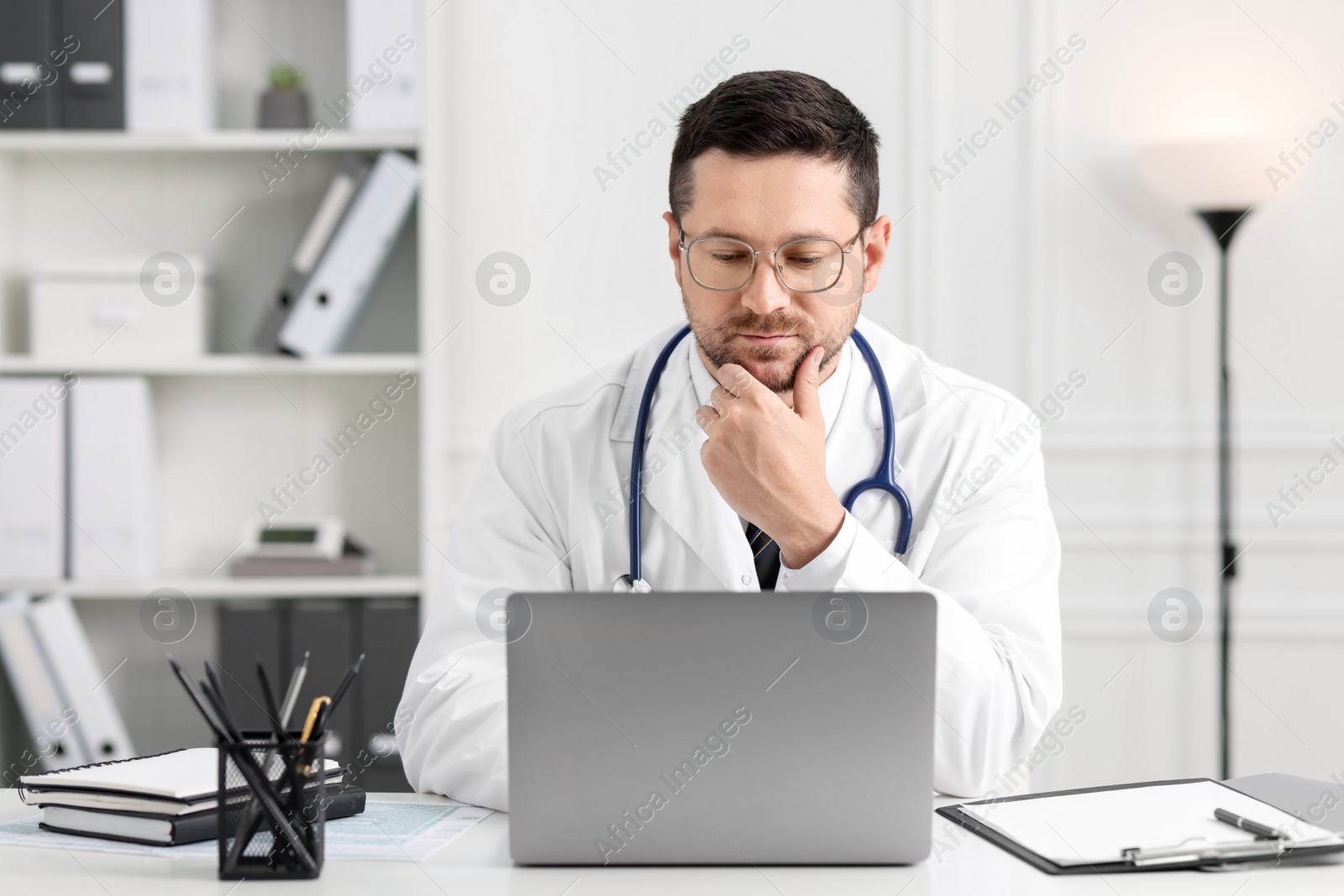 Photo of Doctor having online consultation via laptop at table in clinic