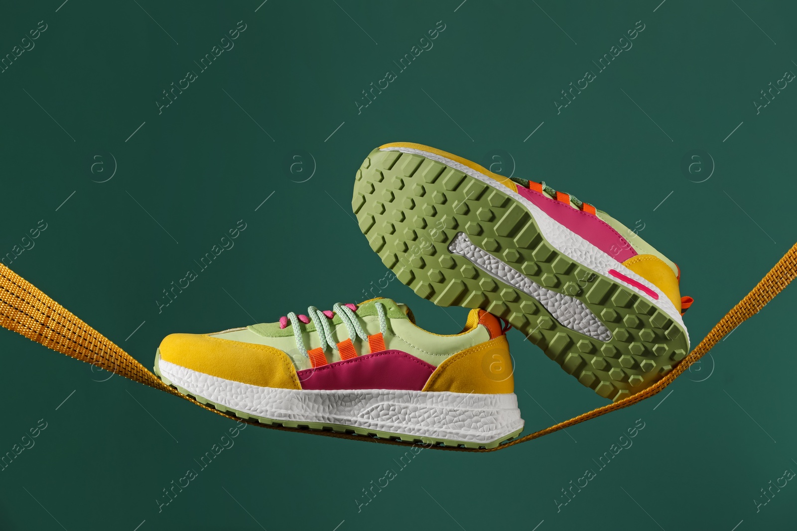 Photo of Pair of stylish colorful sneakers on rope against green background