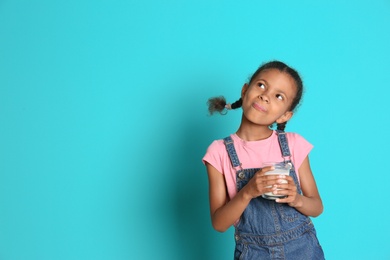 Adorable African-American girl with glass of milk on color background