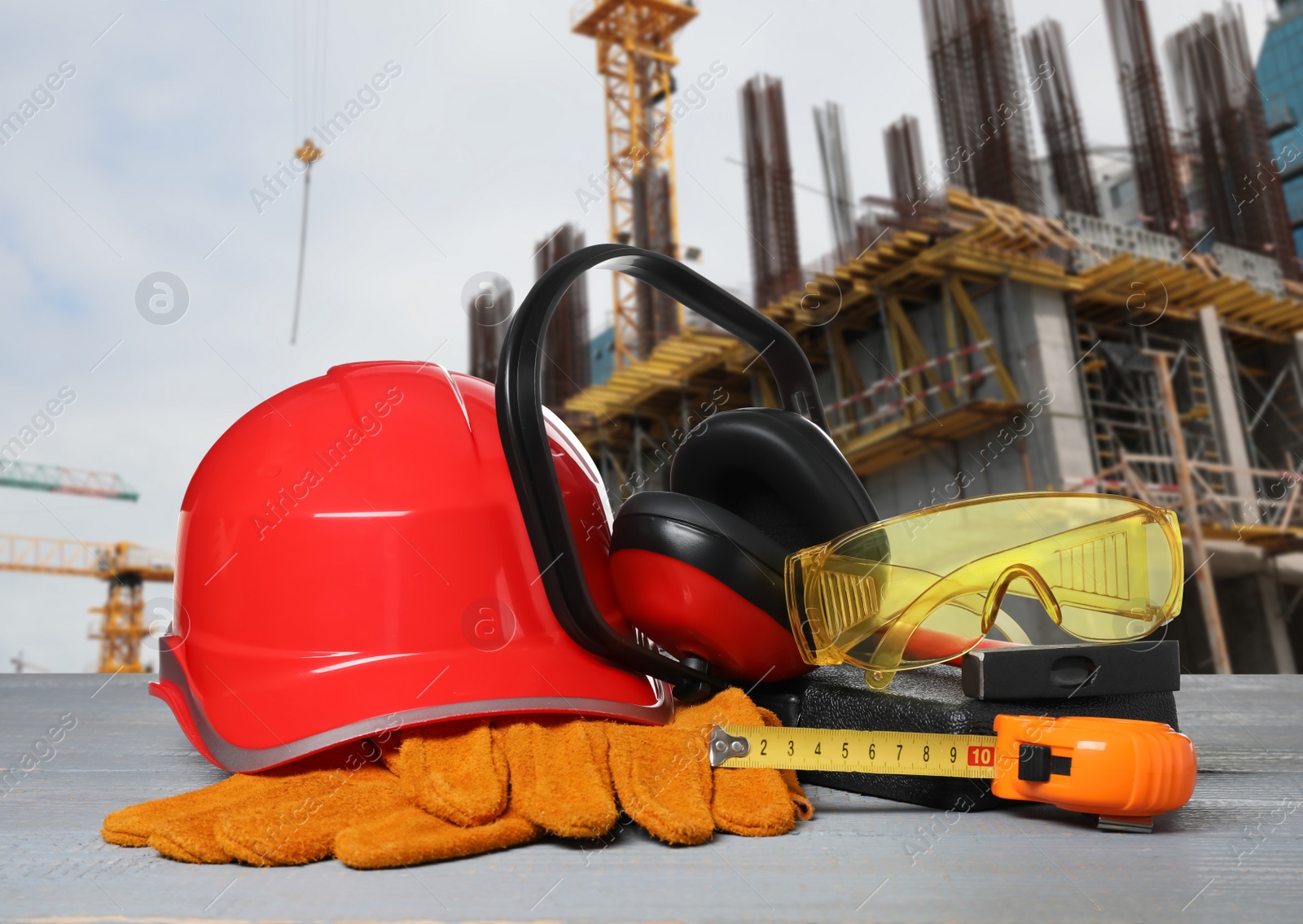 Image of Safety equipment and tools on wooden surface and blurred view of construction site