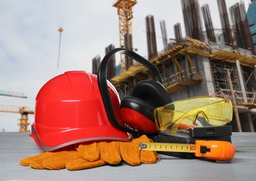 Image of Safety equipment and tools on wooden surface and blurred view of construction site