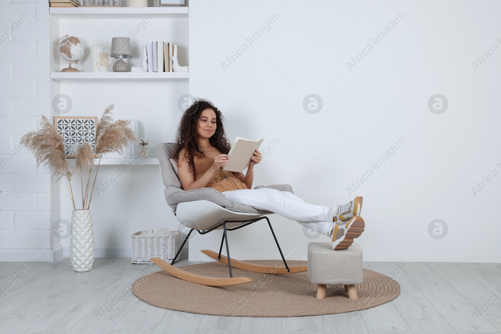 Photo of Young African-American woman reading book in rocking chair at home