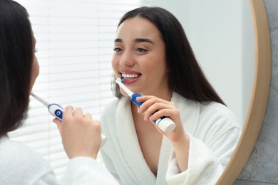 Young woman brushing her teeth with electric toothbrush near mirror in bathroom