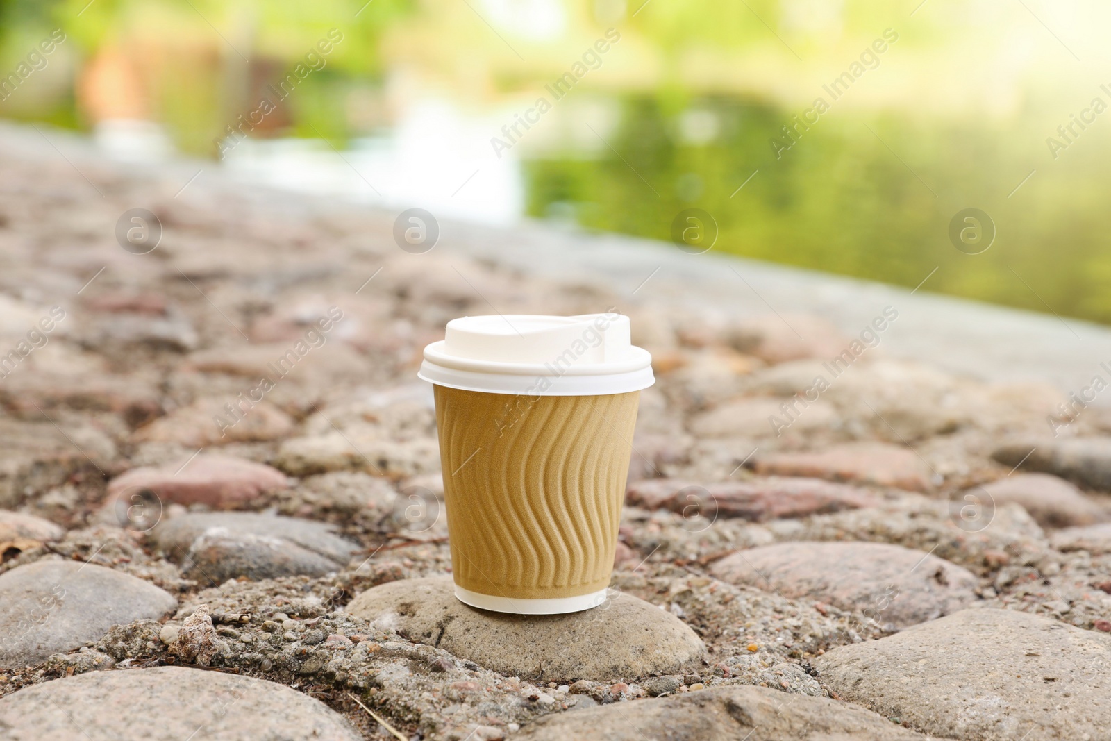 Photo of Paper cup on rocky ground outdoors, space for text. Coffee to go