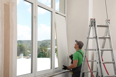 Worker in uniform installing double glazing window indoors