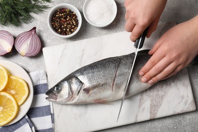 Woman cutting fresh raw sea bass fish at light gray table, closeup