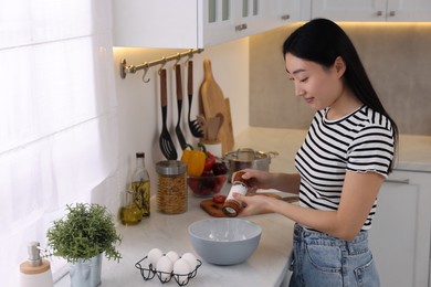 Photo of Cooking process. Beautiful woman adding salt into bowl in kitchen