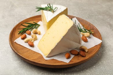 Photo of Plate with pieces of tasty camembert cheese, nuts and rosemary on grey textured table, closeup