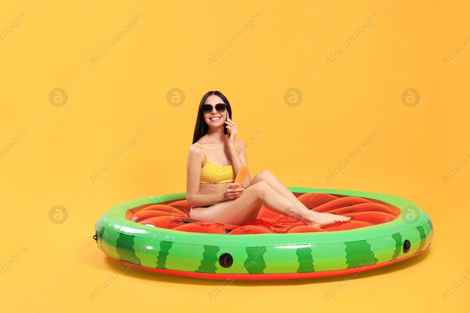 Photo of Happy young woman with beautiful suntan and sunglasses on inflatable mattress against orange background