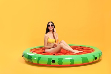 Happy young woman with beautiful suntan and sunglasses on inflatable mattress against orange background