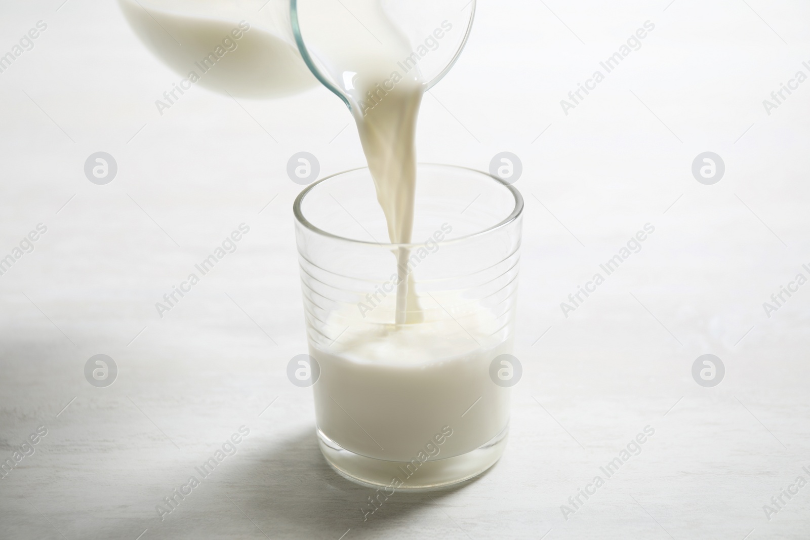 Photo of Pouring milk into glass on white table