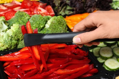 Young woman taking sliced red bell peppers from salad bar, closeup