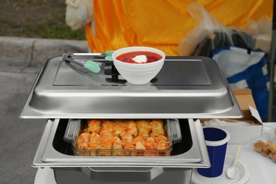 Photo of Volunteer food distribution. Metal warmer with tasty stuffed cabbage on white table outdoors