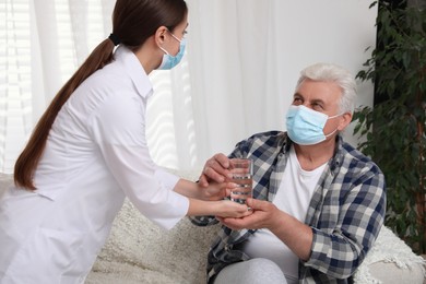 Photo of Doctor giving water to senior man with protective mask at nursing home