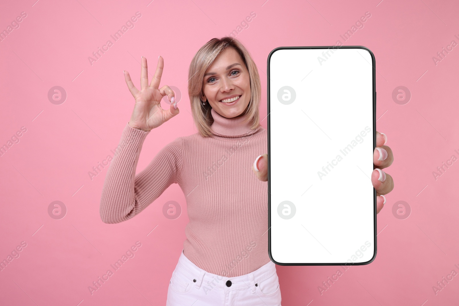 Image of Happy woman showing mobile phone with blank screen on pink background. Mockup for design