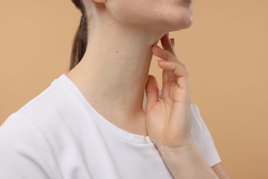 Woman touching her neck on beige background, closeup